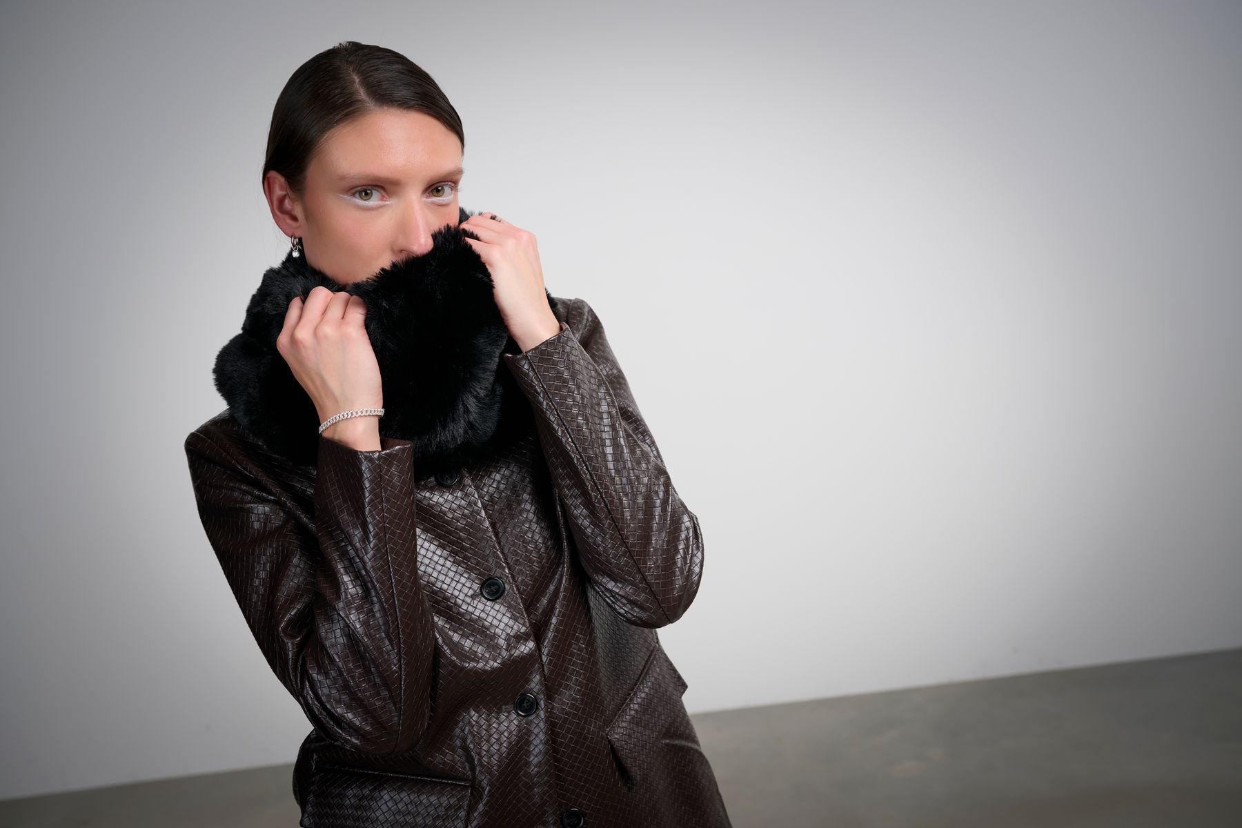 Model in Lederjacke mit schwarzem Schal vor hellem Hintergrund